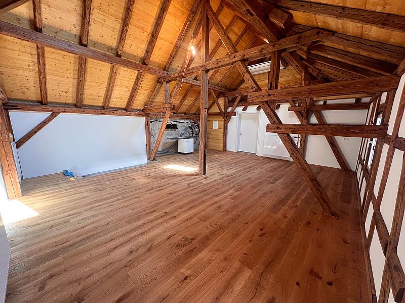 4afb3080-d0f2-4ad8-b4dc-bc523c8313fc Ein geräumiger Dachboden mit Sichtbalken und neu verlegtem Parkettboden strahlt rustikalen Charme aus.